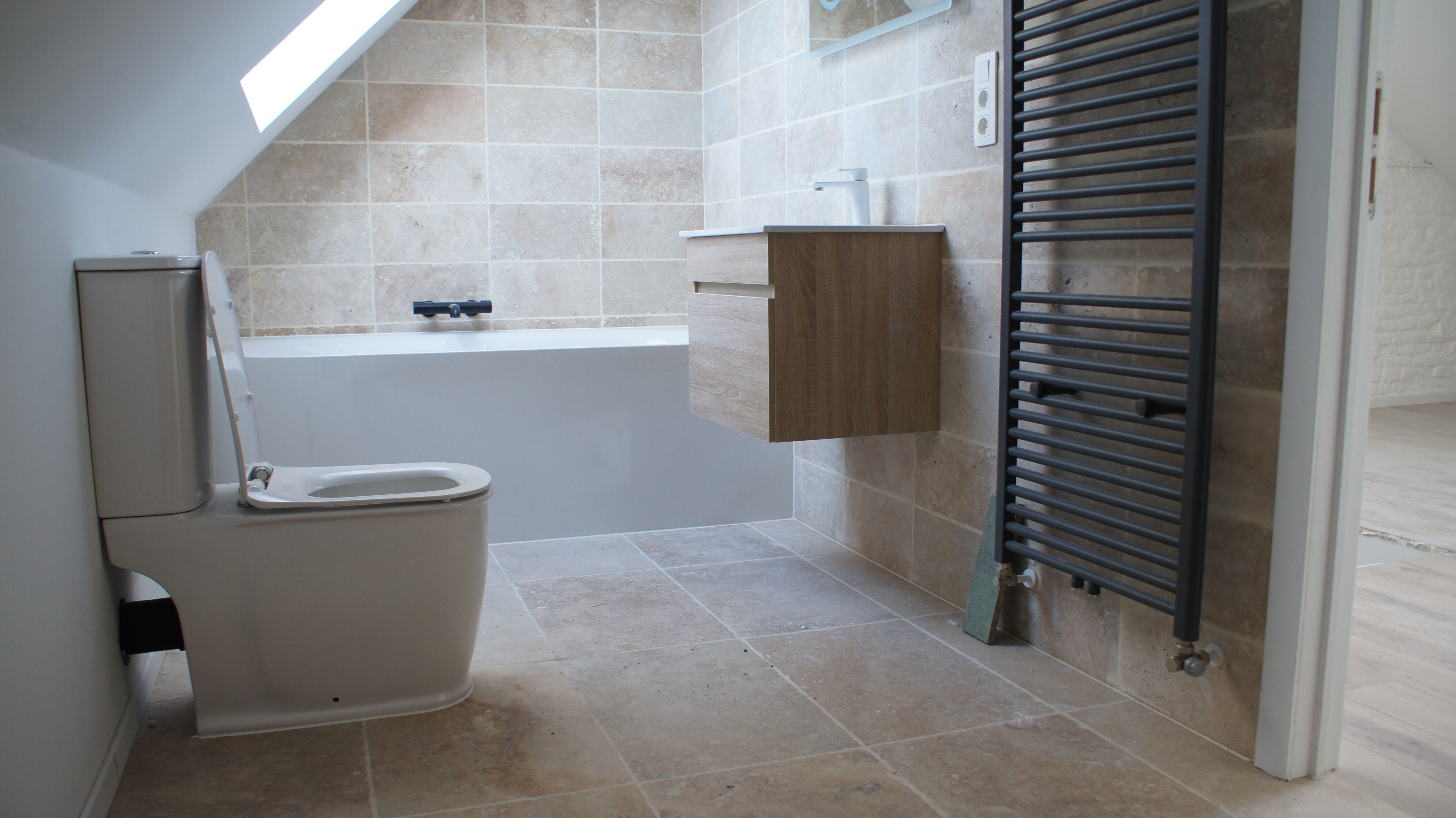 Salle de bains rénovée en travertin avec baignoire et meuble bois suspendu
